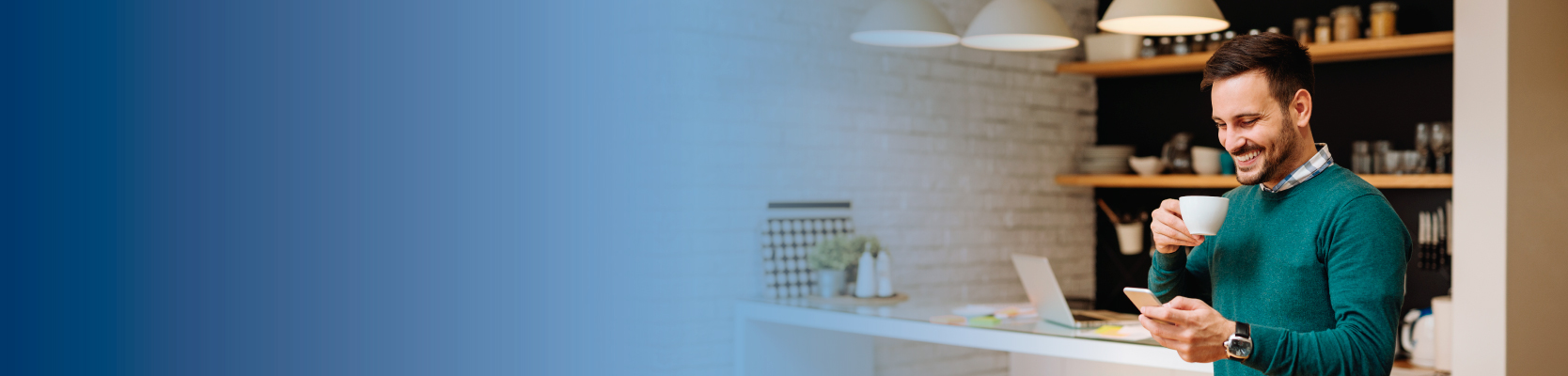 Imagen de un hombre sonriendo mientras ve su teléfono móvil y toma un café en la cocina