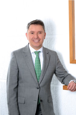 Hombre sonriendo con un traje gris claro y corbata verde